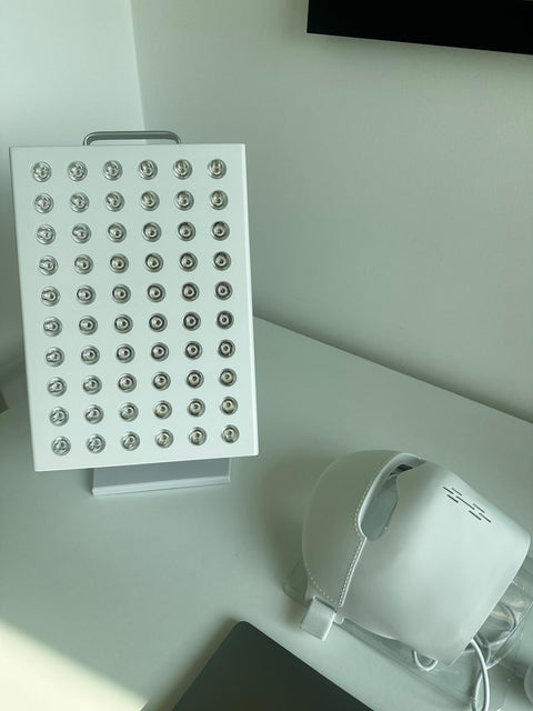 White red light therapy panel with multiple LED bulbs on a desk, next to a white chair and a potted plant, in a modern office setting