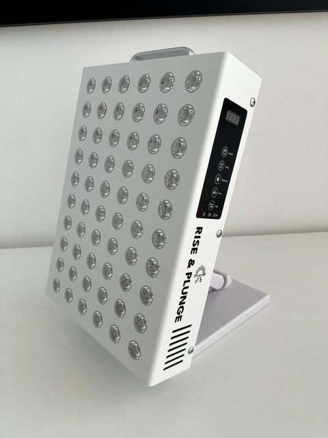 Close-up of white red light therapy panel with digital display and control buttons, on a desk with a white wall background